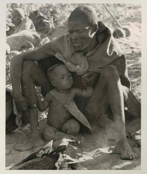 Visiting man sitting with his child between his knees at a fire
