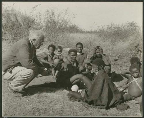 [No folder title]: Gau, "Old ≠Toma," /Gam and //Khuga (wife of !Naishi) sitting with Laurence Marshall (print is a cropped image)