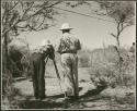 [No folder title]: Lorna Marshall filming a group of people, with Laurence Marshall standing next to her, view from behind (print is a cropped image)