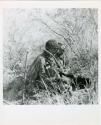 Digging for roots: Woman sitting next to a hole from which she has dug up a root