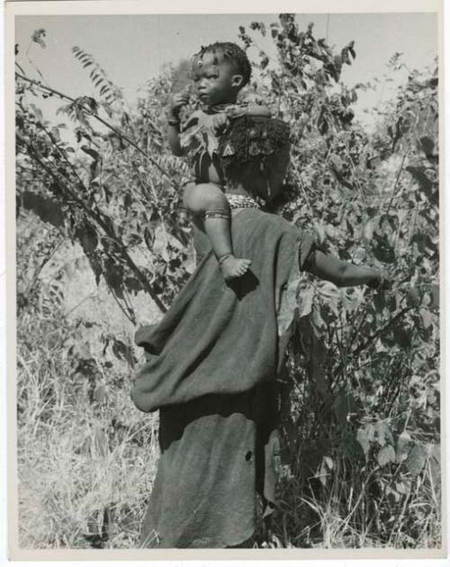 Berry picking: Woman holding a child on her shoulder while she picks berries, view from behind (print is a cropped image)