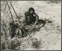 Tsi gathering: Woman from /Ti!kay's group sitting, with a pile of tsi, bags and digging stick on the ground near her (print is a cropped image)