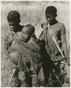 [No folder title]: Tsekue carrying and nursing N!whakwe, with DaSi!Na standing behind them (print is a cropped image)