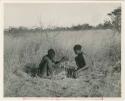 [No folder title]: ≠Gao (headman of Band 3) and "/Qui Hunter" making a fire, with ≠Gao twirling the "male" stick in the notch of the "female" stick, steadying it with his digging stick and his foot (print is a cropped image)