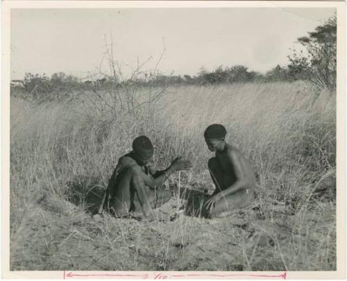 [No folder title]: ≠Gao (headman of Band 3) and "/Qui Hunter" making a fire, with ≠Gao twirling the "male" stick in the notch of the "female" stick, steadying it with his digging stick and his foot (print is a cropped image)