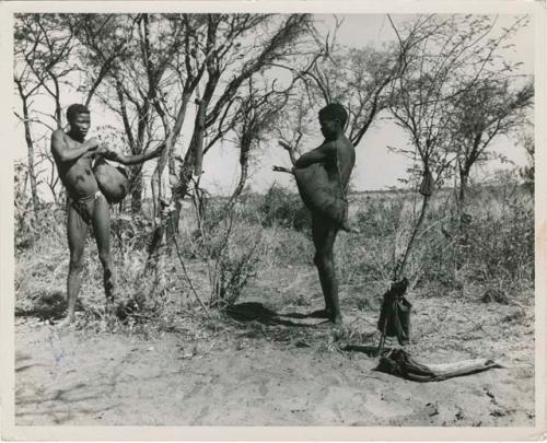 Tsi: Two men standing and holding skin bags full of tsi over their shoulders (print is a cropped image)