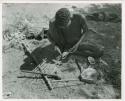 Hunters walking, standing: "Gao Medicine" applying poison with a stick to the shaft of an arrow (print is a cropped image)