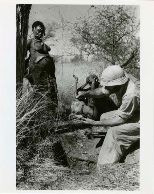 "[Robert] Story, gathering photos": //Kushay standing next to Robert Story sitting pulling out a root (print is a cropped image)