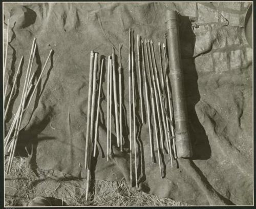 Hunting equipment:  Quiver with contents laid out on a kaross, including arrow shafts without points, "male" and "female" fire-sticks, two drills, two long arrows with unbarbed points, an arrow-shaft, and six arrows with metal points (print is a cropped image)