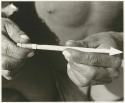 Hunting equipment: Person's hands holding larva and a little stick smeared with poison (print is a cropped image)