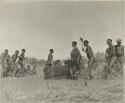 Group of men performing a curing dance, with an elderly woman (/Gam) dancing in the center