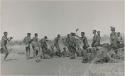 Group of men performing a curing dance, including /Gam dancing in the middle and a young man dancing behind her