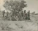 Group of men performing a curing dance, with a circle of women sitting