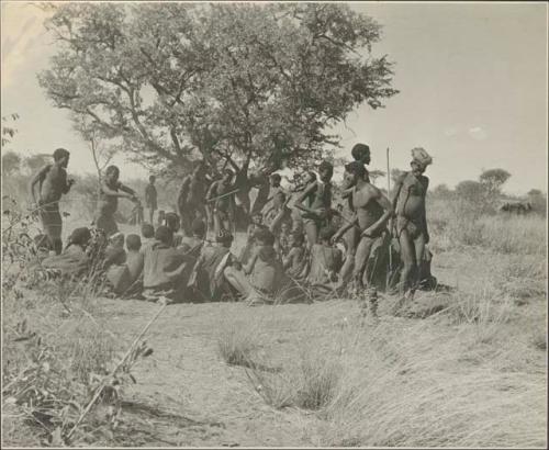 Group of men performing a curing dance, with a circle of women sitting