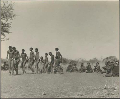 Men performing a curing dance, with a group of women sitting and clapping