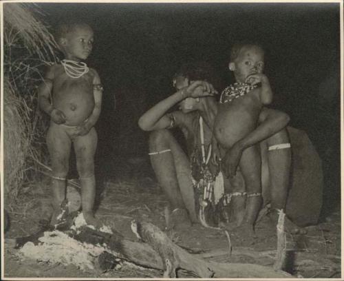 Two women sitting next to a fire in front of a skerm at night, with two children standing next to them