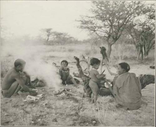 Group of people including ≠Toma sitting by a smoking fire