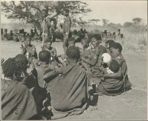 /Naoka giving a drink of water her child while sitting with women in the dance circle
