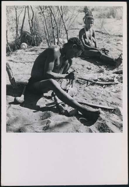 "Gao Helmet" shaping an assegai blade, with his second wife //Kushay