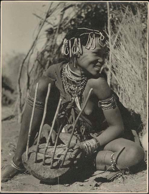 Khuan//a (daughter of !Naishi, headman of Band 5, and //Khuga) sitting in front of a skerm, playing a //guashi