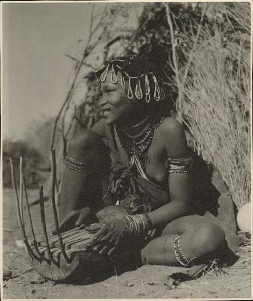 Khuan//a (daughter of !Naishi, headman of Band 5, and //Khuga) sitting in front of a skerm, playing a //guashi