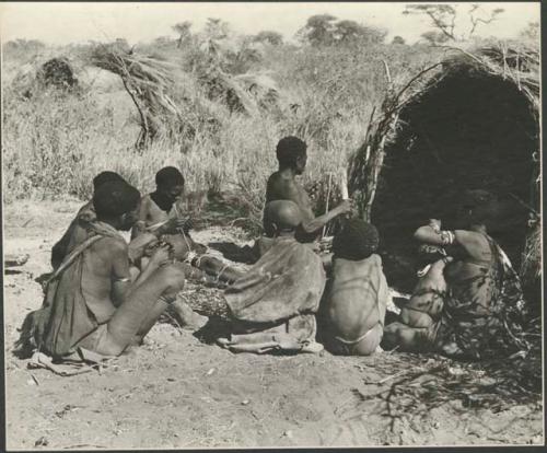 Two women and a child work with nuts near a shelter skerm
