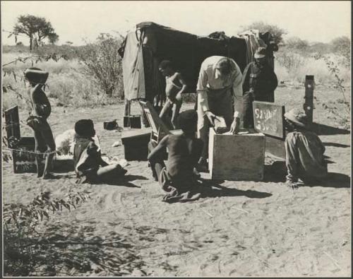 Hans Ernst tending to sound equipment at the sound tent, with a group of Ju/'hoansi watching