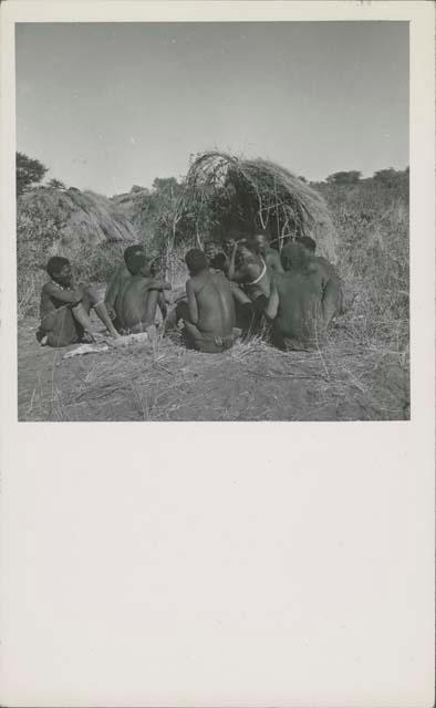 Group of people sitting in front of a skerm, telling stories, including Zuma (daughter of "Old Xama," wife of Gao), Xama, Gao (son of Debe, headman of Band 24 in Cho/ana) and /Qui (brother of "Gao Helmet")