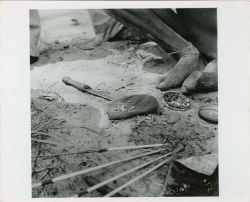 [No folder title]: Poison grubs used for arrows in the top of a shoe polish tin next to a man's feet (print is a cropped image)