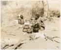 [No folder title]: Child drinking from an ostrich eggshell and a woman (likely /Naoka, U!'s mother) sitting beside a fire with a pot and bones before her (print is a cropped image)