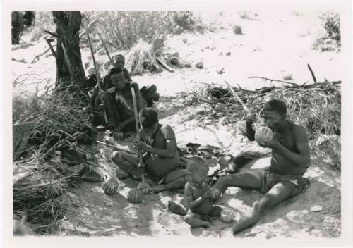 "With tsama": !Gai's family eating tsama melons (Back to front, left to right: //Ku≠tera, /Twikwe, Tsekue, N!whakwe, and !Gai) (print is a cropped image)