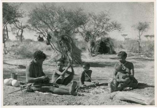 [Baobab tree]: ≠Toma working on arrows and sitting with his family members Tsamgao, /Gaishay, and !U holding !Ungka Norna (print is a cropped image)