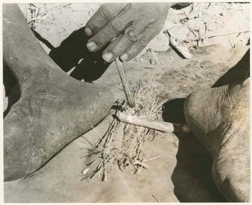 "Firemaking": Firesticks held in position for fire making (print is a cropped image)