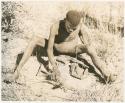 "Firemaking": Man adding grass to tinder pile (print is a cropped image)