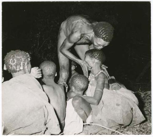 "Night dance at Tsumkwe 1957-8, some published in my [Lorna Marshall's] dance paper": Medicine man leaning over, curing a woman sitting with a group of women and children (print is a cropped image)