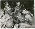 "Night dance at Tsumkwe 1957-8, some published in my [Lorna Marshall's] dance paper": Medicine man leaning over a circle of women and children clapping (print is a cropped image)