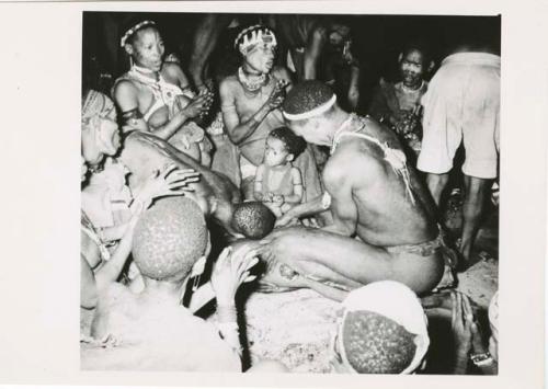 "Night dance at Tsumkwe 1957-8, some published in my [Lorna Marshall's] dance paper": Medicine man leaning over a circle of women and children clapping (print is a cropped image)