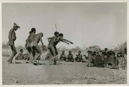 "Daytime dance at Gautscha": Group of men dancing through a circle of women sitting, one man's arms outstretched (print is a cropped image)