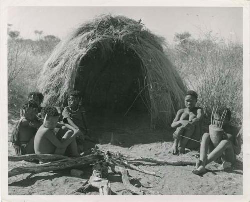 "N!ai and /Gunda": "Little N!ai" and /Gunda (son of Khwan//a and her former husband) sitting by their skerm with their wedding party, including Tsamgao (son of ≠Toma and !U), ≠Gisa (daughter of ≠Gao and Khwo//o-/Gasa), Xama (daughter of "Gao Helmet" and //Kushay), ≠Gao (son of Gau and Be), and a boy playing the //guashi (print is a cropped image)