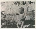 N!whakwe crying, holding a small turtle and a tin in his hands


