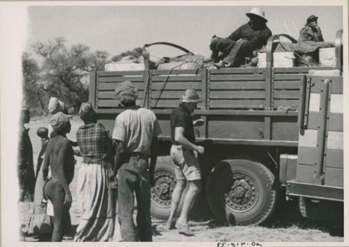 Group of people standing around expedition truck, men sitting inside truck (image partly obscured)



