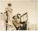 Heinrich Neumann standing, and Wilhelm Camm and Casper Kruger sitting inside an expedition truck



