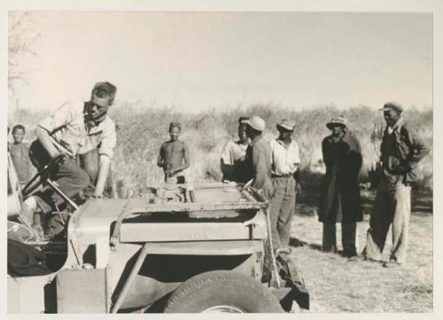 Group of people standing, and John Marshall climbing into the expedition Jeep


