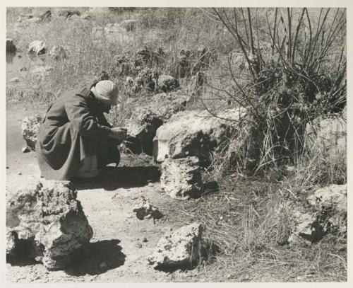 Robert Story wearing an overcoat and crouching to look at something


