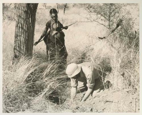 //Kushay standing next to Robert Story kneeling beside a deep hole


