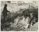 ≠Toma standing with a shovel, and Elizabeth Marshall Thomas bending over a bundle of grass, clearing the camp site

