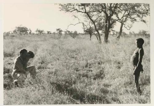 Gao, father of N!aba, standing and posing, and William Donellan photographing him
