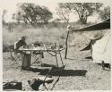 Robert Story sitting at a table in the expedition camp at tea-time
