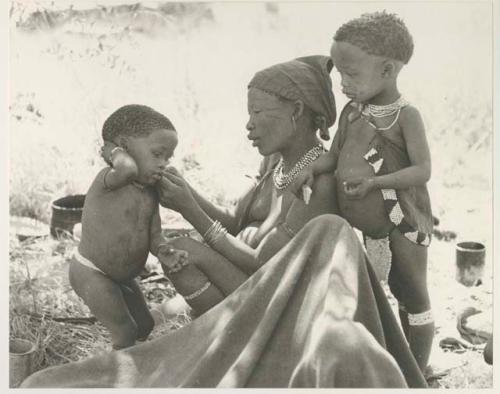 Debe standing beside !U, who is fixing his beads; and Norna leaning against her mother's shoulder