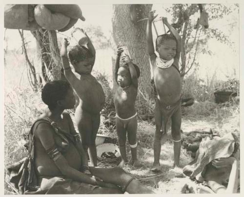 //Khuga sitting, and her daughter Bau, and Di!ai's sons Debe and /Gaishay holding tins on their heads